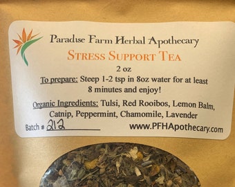 Puede incluir: Una bolsa de papel marrón con una etiqueta que dice "Paradise Farm Herbal Apothecary Stress Support Tea 2 oz". La etiqueta también incluye instrucciones para preparar el té y una lista de ingredientes orgánicos: Tulsi, Rooibos rojo, melisa, hierba gatera, menta piperita, manzanilla y lavanda. La bolsa tiene una ventana transparente que muestra la mezcla de té de hojas sueltas en el interior.