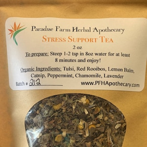May include: A brown paper bag with a label that reads "Paradise Farm Herbal Apothecary Stress Support Tea 2 oz". The label also includes instructions for preparing the tea and a list of organic ingredients: Tulsi, Red Rooibos, Lemon Balm, Catnip, Peppermint, Chamomile, and Lavender. The bag has a clear window showing the loose leaf tea blend inside.