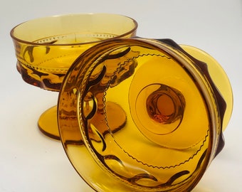 May include: Two amber glass dessert dishes with a scalloped edge and a decorative pattern. The dishes are turned upside down, showing the bottom of the dishes.