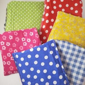 May include: A selection of patterned fabric squares in a variety of colours. The fabrics feature polka dots in red, blue, and green, floral designs in pink and yellow, and a blue and white gingham check. The squares are neatly arranged.