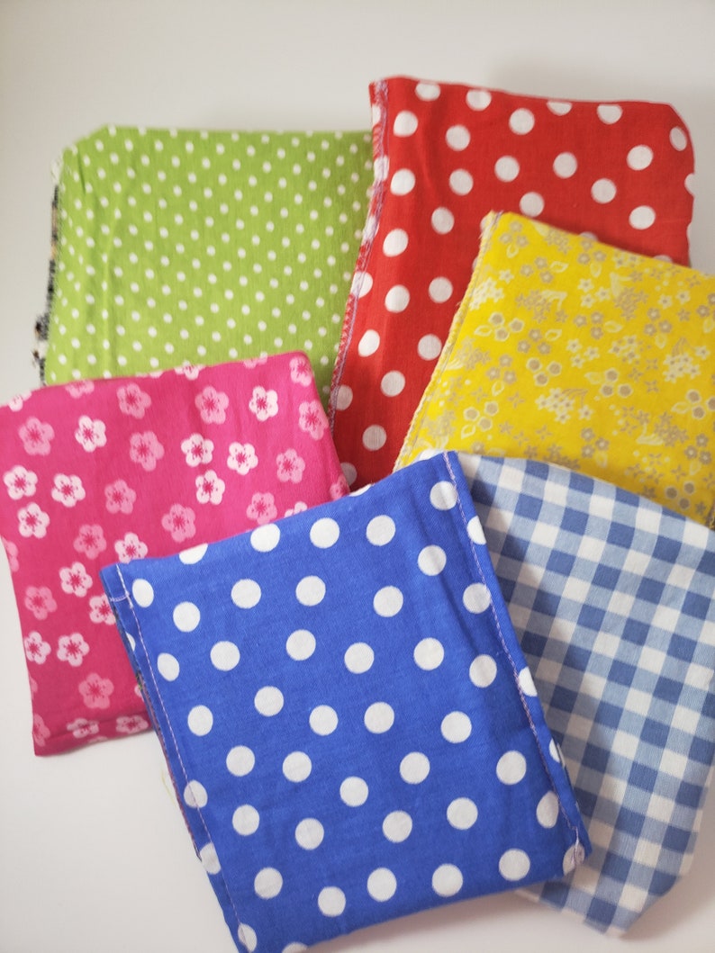May include: A selection of patterned fabric squares in a variety of colours. The fabrics feature polka dots in red, blue, and green, floral designs in pink and yellow, and a blue and white gingham check. The squares are neatly arranged.