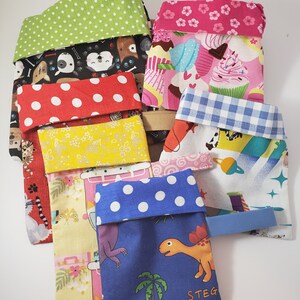 May include: A selection of patterned fabric pouches. Designs include polka dots, cupcakes, dogs, and dinosaurs. Each pouch has a contrasting, folded-over top. Some have a small fabric tab.