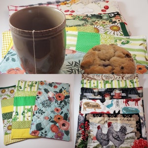 May include: A brown mug with a tea bag, a chocolate chip cookie, and several quilted fabric coasters with floral, farm, and patchwork designs. The coasters are in various colors, including green, yellow, and blue.