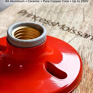 Puede incluir: Un casquillo de lámpara E27 de montaje en superficie de color rojo brillante con exterior de aluminio, anillo interior de cerámica y núcleo de cobre puro. El texto E27 Surface Mount Lamp Socket, All-Aluminum, Ceramic, Pure Copper Core, Up to 250V es visible.