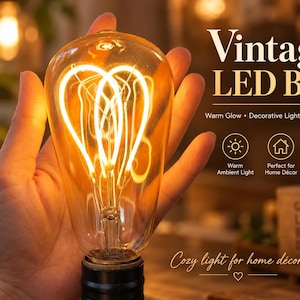 May include: A clear glass vintage LED bulb with a warm glowing heart-shaped filament. The text reads: Vintage LED Bulb, Warm Glow, Decorative Lighting, E26/E27, Warm Ambient Light, Perfect for Home Décor, Energy Efficient LED, Cozy light for home décor.