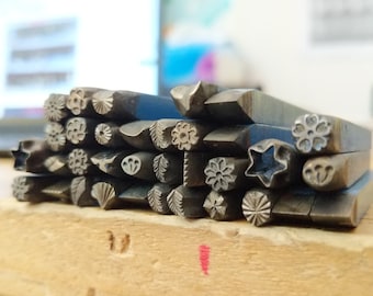 May include: A collection of metal stamps with various designs, including flowers, stars, and leaves. The stamps are arranged in a stack on a wooden surface.