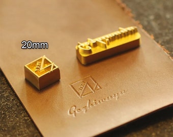 May include: Two gold-colored metal stamps for leather crafting. The larger stamp is rectangular and reads "Gephiwrapper". The smaller stamp is square and measures 20 mm. Both stamps feature a geometric design.