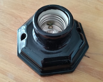 May include: Black ceramic light socket with a standard screw-in base. The socket has a hexagonal shape and is designed for use with standard light bulbs.