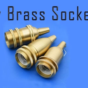 Puede incluir: Tres portalámparas de latón de color dorado sobre un fondo azul. Los portalámparas son de diferentes tamaños y tienen un diseño roscado.