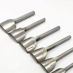 May include: Set of six silver metal leather hole punches with curved edges. The punches are arranged in a row, with the largest punch at the top and the smallest punch at the bottom.