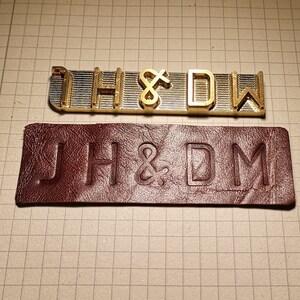 May include: A close-up of a metal stamp set with the letters "JH&DM" and a leather stamp with the same letters embossed on it.