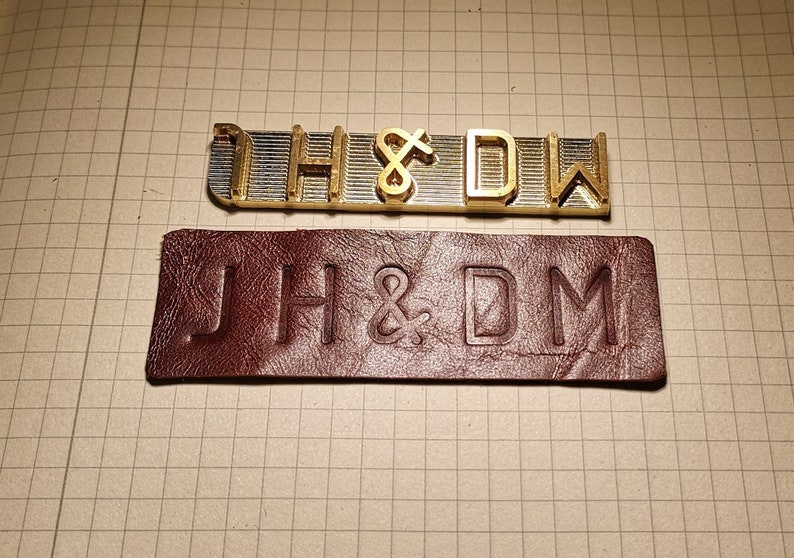 May include: A close-up of a metal stamp set with the letters "JH&DM" and a leather stamp with the same letters embossed on it.