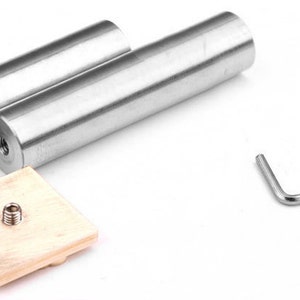 May include: Two cylindrical silver-toned metal rods with threaded ends, a square light-colored wooden base with a central metal screw, a small L-shaped hex key, and a single small threaded metal screw component for assembly and hardware use.