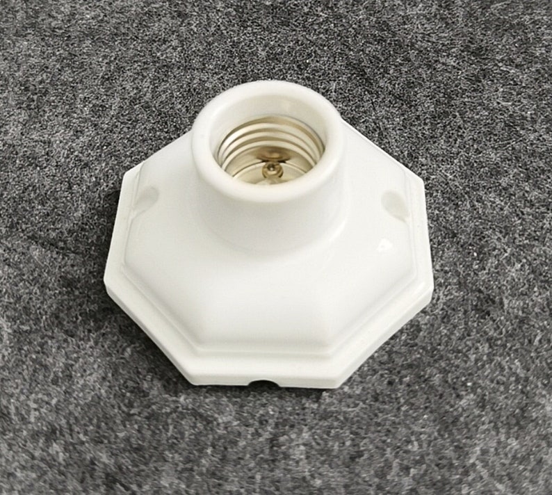 May include: White ceramic light bulb socket with a standard screw-in base. The socket has a hexagonal shape and is designed for indoor use.