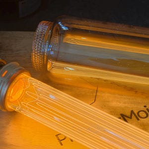 May include: Close-up of a vintage-style light bulb with a warm, amber glow. The bulb has a clear glass tube with a filament design. The base is metallic, and the bulb is partially lit, creating a cozy ambiance.