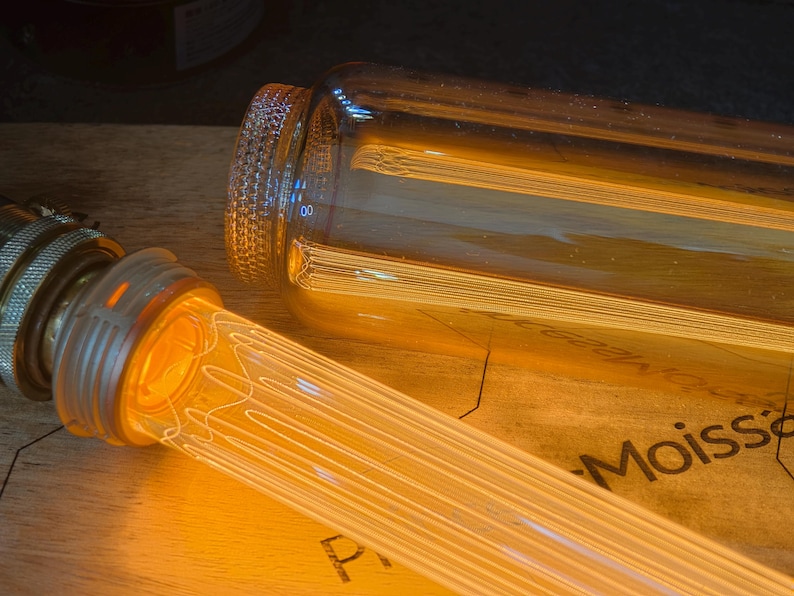 May include: Close-up of a vintage-style light bulb with a warm, amber glow. The bulb has a clear glass tube with a filament design. The base is metallic, and the bulb is partially lit, creating a cozy ambiance.