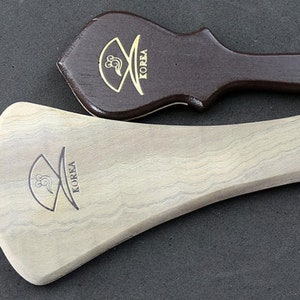 May include: Two wooden paddles with a curved shape and a handle. Both paddles have the word "KOREA" engraved on them.