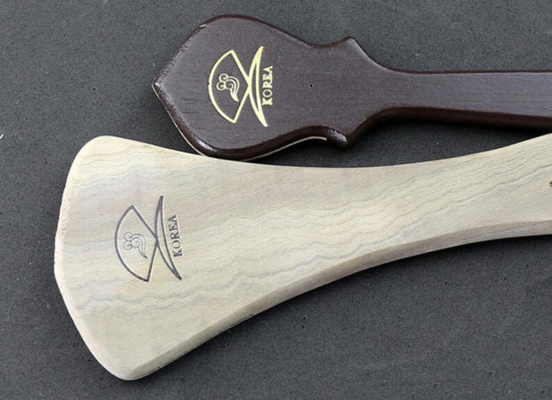 May include: Two wooden paddles with a curved shape and a handle. Both paddles have the word "KOREA" engraved on them.