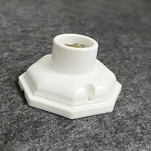 May include: White ceramic light socket with a hexagonal base. The socket has a threaded opening for a light bulb.