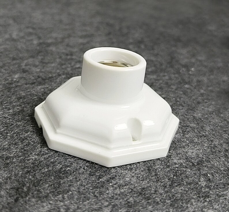 May include: White ceramic light socket with a hexagonal base. The socket has a threaded opening for a light bulb.
