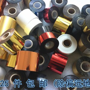 May include: Assortment of gold, silver, and black ribbon rolls. The rolls are various sizes and are arranged in a pile.