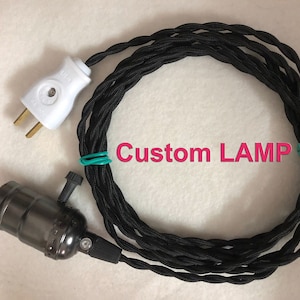 May include: Black electrical cord with a white plug on one end and a black metal light socket on the other end. The cord is coiled and the text "Custom LAMP" is visible in the centre of the image.
