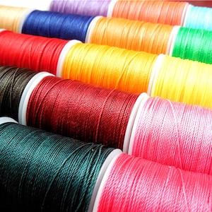 May include: Spools of colorful thread in various shades of red, orange, yellow, green, blue, purple, brown, and pink. The thread is wound around white plastic spools.