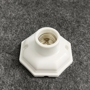 May include: White ceramic light socket with a standard screw-in base. The socket has a hexagonal shape and is designed for indoor use.