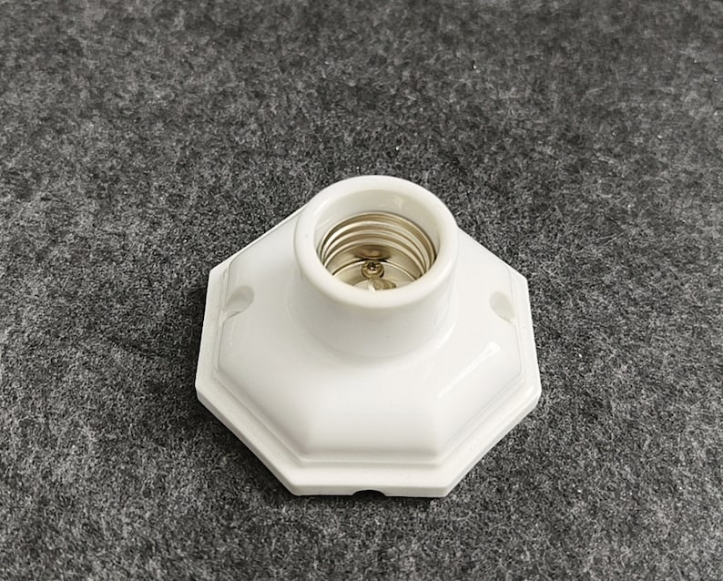 May include: White ceramic light socket with a standard screw-in base. The socket has a hexagonal shape and is designed for indoor use.