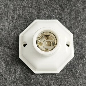 May include: White porcelain light socket with a gold-colored center. The socket is octagonal in shape.