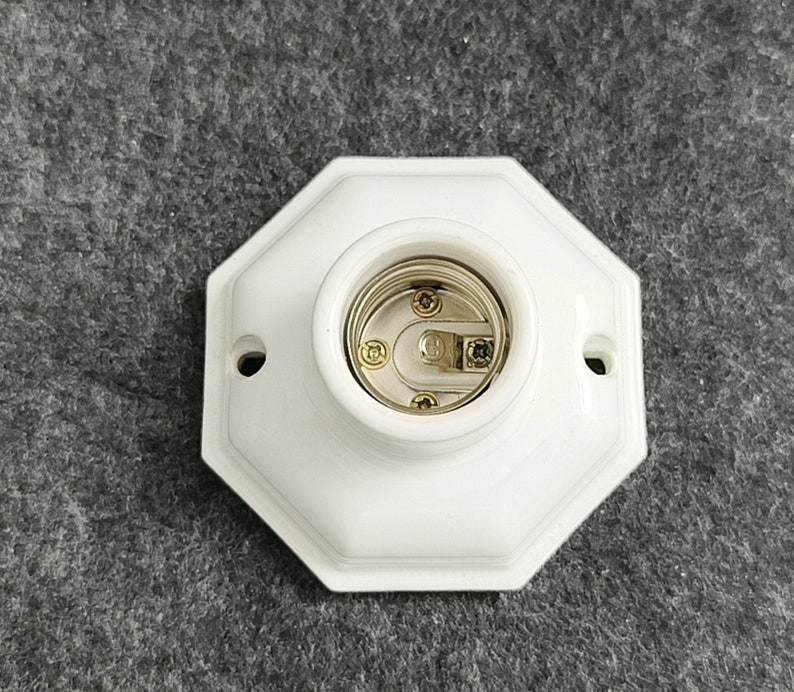 May include: White porcelain light socket with a gold-colored center. The socket is octagonal in shape.