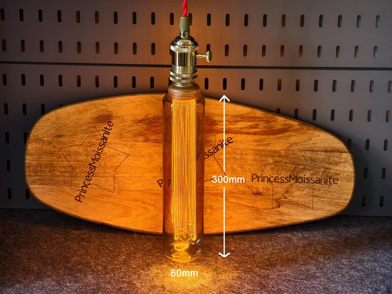 May include: A vintage-style light fixture with a clear glass bulb, 300mm in length, and a brass base. The bulb is filled with vertical filaments. The fixture is suspended by a red cord. The fixture is placed in front of a wooden board with the text "PrincessMoissanite".