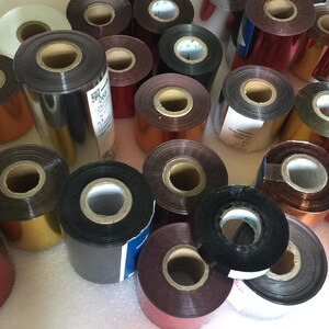 May include: Assortment of colorful foil ribbon rolls for a hot stamping machine. The rolls are various colors, including gold, silver, red, and black.