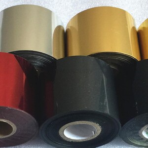 May include: Assortment of rolls of metallic foil in various colors, including gold, silver, red, black, and white. The rolls are stacked on top of each other.