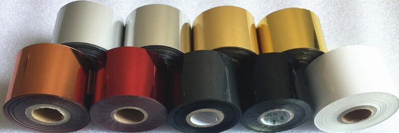 May include: Assortment of rolls of metallic foil in various colors, including gold, silver, red, black, and white. The rolls are stacked on top of each other.