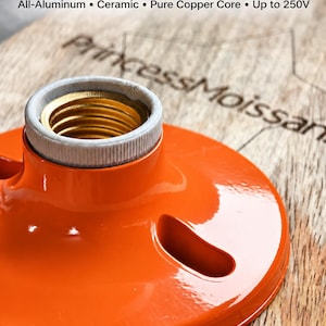 May include: An orange E27 surface mount lamp socket with a ceramic interior and a gold-colored threaded metal core. The text reads: E27 Surface Mount Lamp Socket, All-Aluminum, Ceramic, Pure Copper Core, Up to 250V, and princessMoissan.
