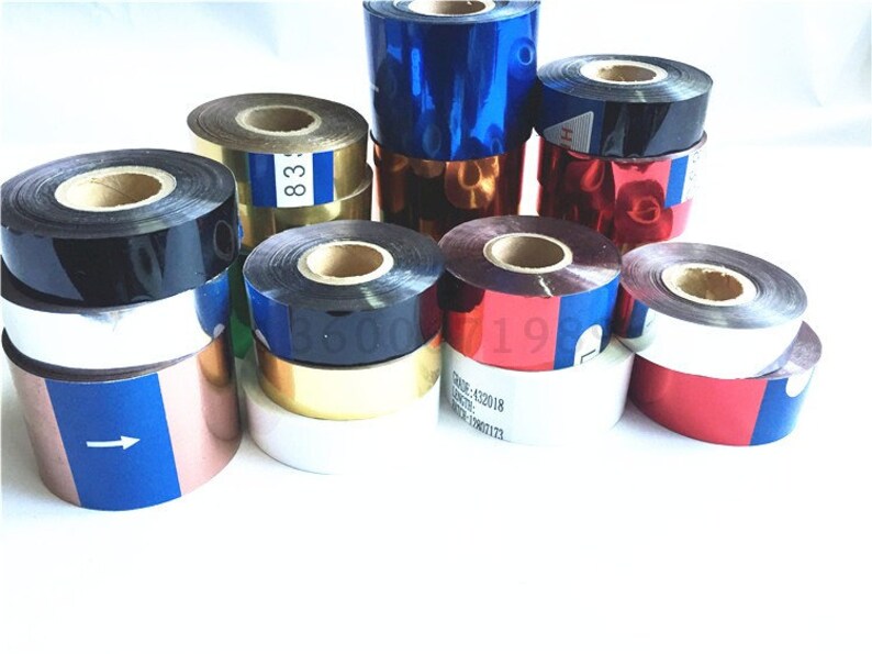 May include: Assortment of colorful ribbon rolls, including black, gold, red, blue, and silver. The rolls are stacked and arranged on a white surface. Some rolls have text printed on them, such as "83" and "19".