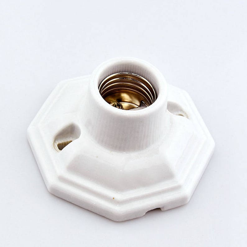 May include: White porcelain light socket with a standard screw-in base. The socket has a hexagonal base with rounded edges.