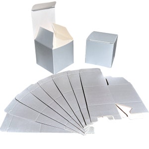 Puede incluir: Un conjunto de 12 cajas de regalo de cartón gris, planas. Las cajas están dobladas y listas para ser ensambladas.