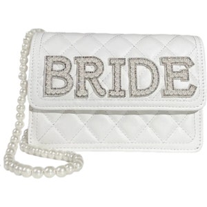May include: White quilted handbag with a pearl chain strap. The front flap has the word "BRIDE" spelled out in large letters with pearl embellishments.