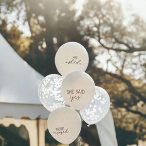 Peut inclure: Ballons blancs avec du texte noir. Les ballons disent "Il a demand&eacute;...", "Elle a dit oui !" et "Nous sommes fianc&eacute;s".