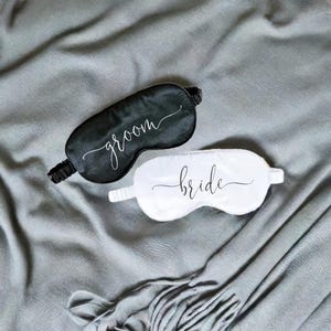 Puede incluir: Un par de antifaces para dormir, uno negro y otro blanco, con las palabras "groom" y "bride" escritas en ellos.