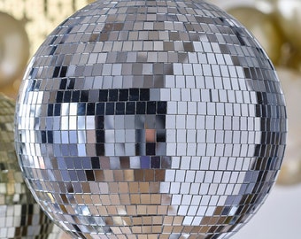 May include: A large silver disco ball with many mirrored tiles. The ball is hanging from a ceiling.
