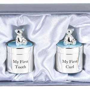 Könnte beinhalten: Zwei silberne Erinnerungsboxen mit blauen Deckeln und Teddybär-Toppern. Die Boxen sind mit "My First Tooth" und "My First Curl" graviert.