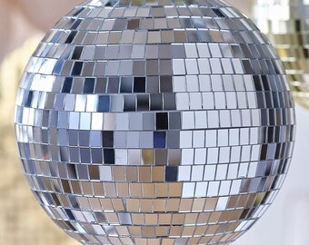 May include: A silver disco ball with a mirrored surface. The ball is round and has many small squares that reflect light.