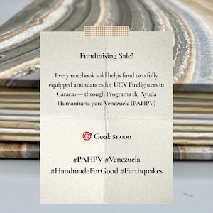 May include: A notebook with a marbled gray and beige cover featuring a cream-colored paper note attached with checkered tape. The text reads: Fundraising Sale! Every notebook sold helps fund two fully equipped ambulances for UCV Firefighters in Caracas — through Programa de Ayuda Humanitaria para Venezuela (PAHPV) Goal: $1,000 #PAHPV #Venezuela #HandmadeForGood #Earthquakes