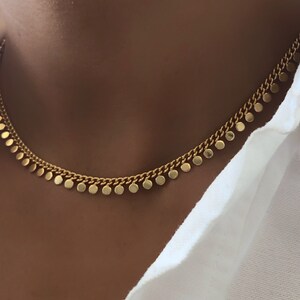 May include: A gold chain necklace with small round charms hanging from it. The necklace is on a person's neck.