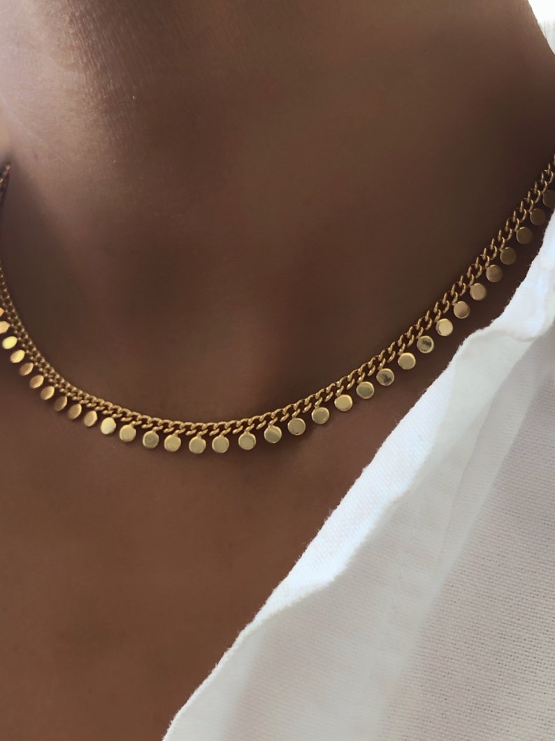 May include: A gold chain necklace with small round charms hanging from it. The necklace is on a person's neck.