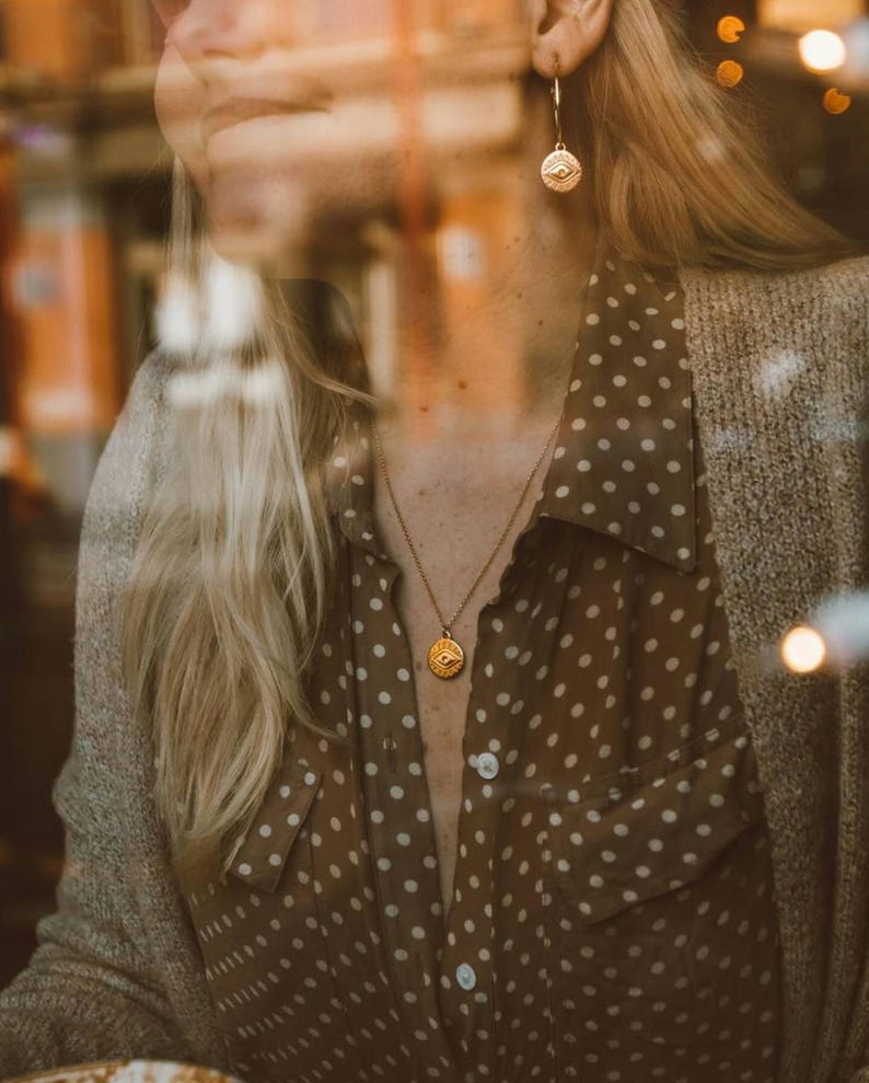 Puede incluir: Una mujer lleva una camisa marr&oacute;n con lunares y un collar y pendientes de oro con un dise&ntilde;o de ojo. El collar y los pendientes son de oro y tienen un dise&ntilde;o simple y elegante.