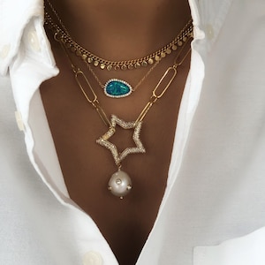 May include: Layered gold necklaces with a blue opal pendant, a star-shaped pendant with clear stones, and a pearl pendant.